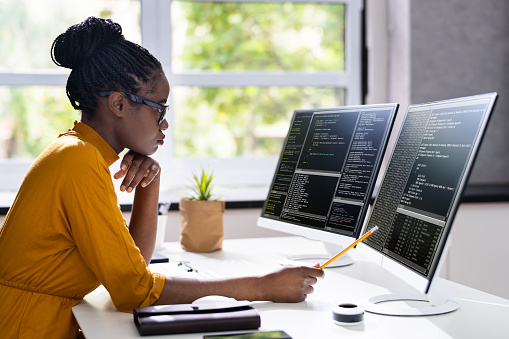 Woman software engineer coding with two screens